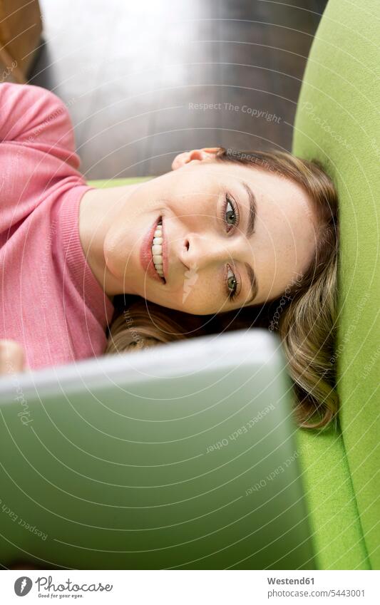 Portrait of smiling woman lying on the couch using tablet laying down lie lying down females women digitizer Tablet Computer Tablet PC Tablet Computers iPad