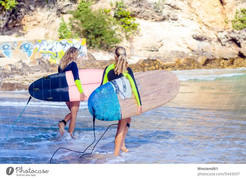 Indonesia, Bali, two women carrying surfboards at the sea surfing surf ride surf riding Surfboarding Sea ocean woman females water sports Water Sport aquatics