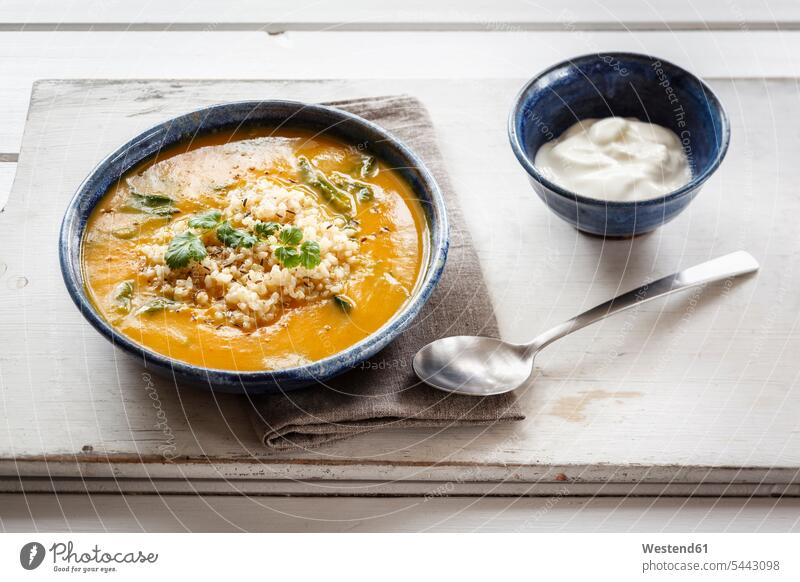 Bowl of creamed pumpkin soup with brown rice and spinach wooden board wooden boards wooden panel wooden panels garnished natural yoghurt plain yoghurt mashed
