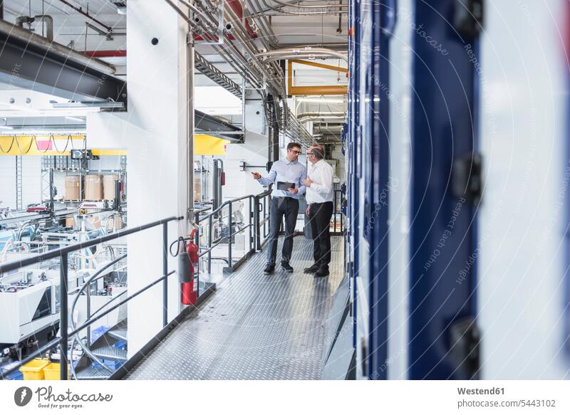 Two men talking in factory shop floor speaking colleagues man males factories Adults grown-ups grownups adult people persons human being humans human beings