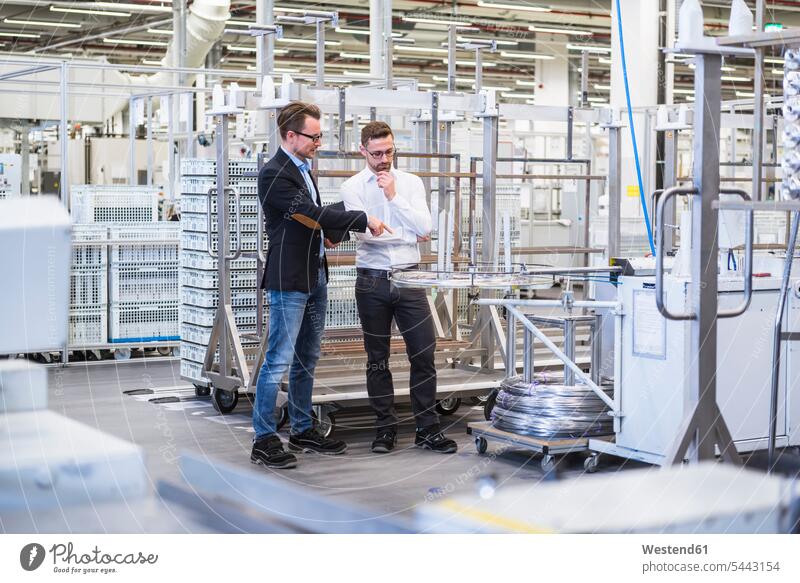 Two men talking in factory shop floor speaking man males factories Adults grown-ups grownups adult people persons human being humans human beings industry