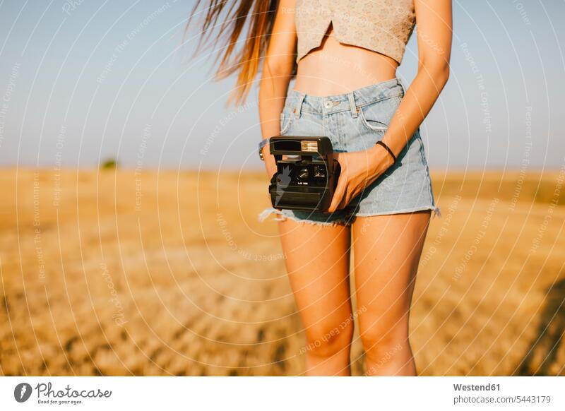 Young woman with instant camera on a field at sunset, partial view females women polaroid camera Adults grown-ups grownups adult people persons human being