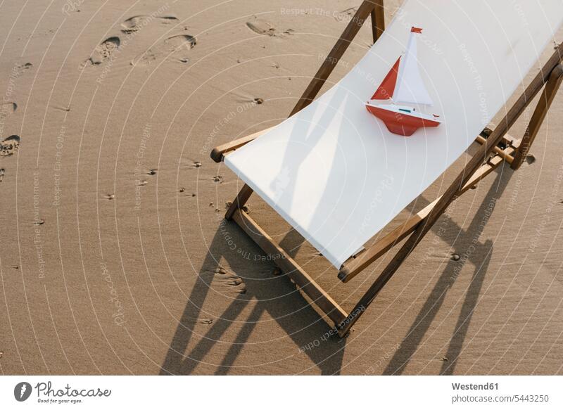 Toy boat in deckchair on the beach deck chair deckchairs deck chairs beaches boats vacation Holidays Travel daylight shot daylight shots day shots daytime