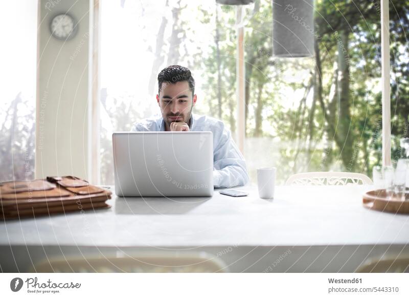 Young businessman sitting in office, using laptop working At Work Laptop Computers laptops notebook desk desks Seated offices office room office rooms reading