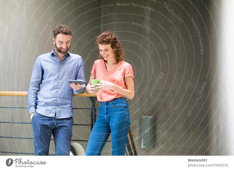 Man and woman in staircase with cell phone and cup of coffee mobile phone mobiles mobile phones Cellphone cell phones smiling smile concrete wall concrete walls