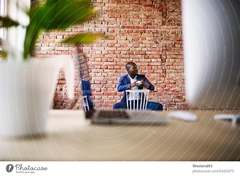 Businessman with cup of coffee sitting on chair in office Coffee Seated chairs Business man Businessmen Business men Drink beverages Drinks Beverage