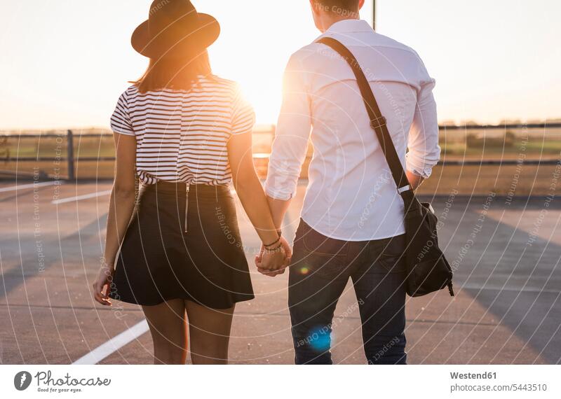 Young couple hand in hand on parking level at sunset sunsets sundown twosomes partnership couples parking garage parking garages parking deck car park