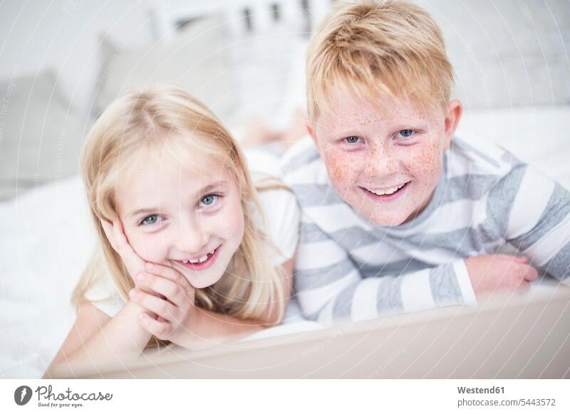 Portait of smiling brother and sister lying in bed with laptop beds brothers sisters smile Laptop Computers laptops notebook siblings brothers and sisters