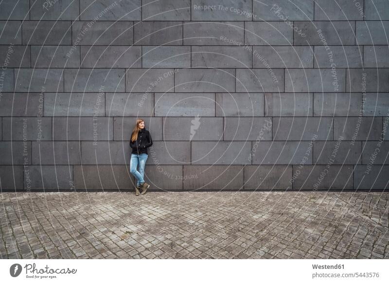 Young woman standing in front of grey facade waiting females women Adults grown-ups grownups adult people persons human being humans human beings appointment