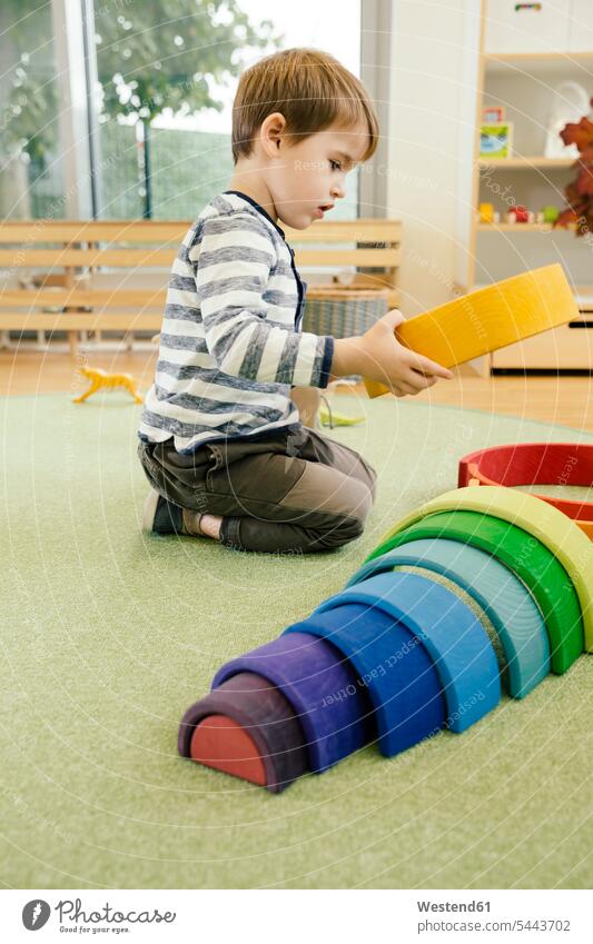 Boy playing with wooden rainbow shapes in kindergarten boy boys males nursery school child children kid kids people persons human being humans human beings