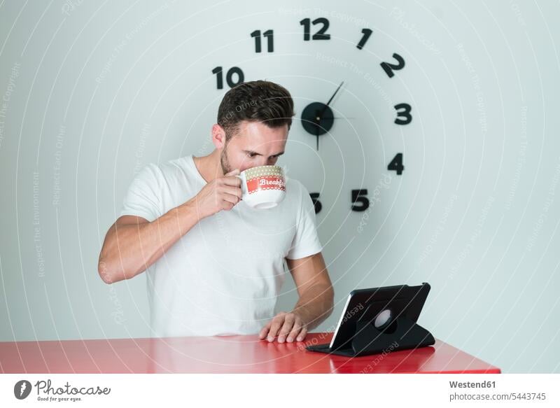 Yong man drinking of a cup and looking his tablet Time Cup Cups watch watches men males digitizer Tablet Computer Tablet PC Tablet Computers iPad Digital Tablet