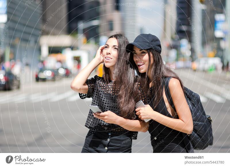 USA, New York City, two happy twin sisters with cell phones in Manhattan mobile phone mobiles mobile phones Cellphone New York State Fun having fun funny