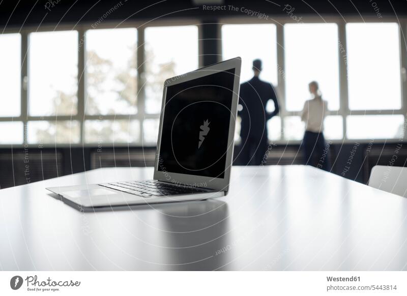 Laptop on table and businessman and businesswoman at the window laptop Laptop Computers laptops notebook businesswomen business woman business women windows