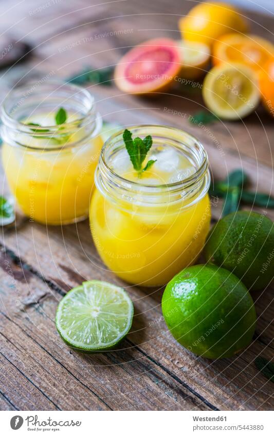 Glass of orange juice, limes, lemon and ice cubes Glasses spice spices Slice Slices half halves halved wooden healthy eating nutrition focus on foreground
