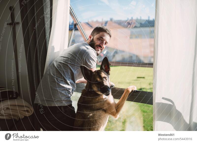 Young man standing at window with his dog, waiting young dogs Canine home at home men males pets animal creatures animals Adults grown-ups grownups adult people