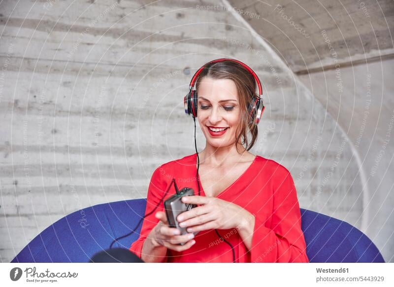 Smiling woman sitting on chair listening to music from walkman headphones headset females women Seated smiling smile hearing Adults grown-ups grownups adult