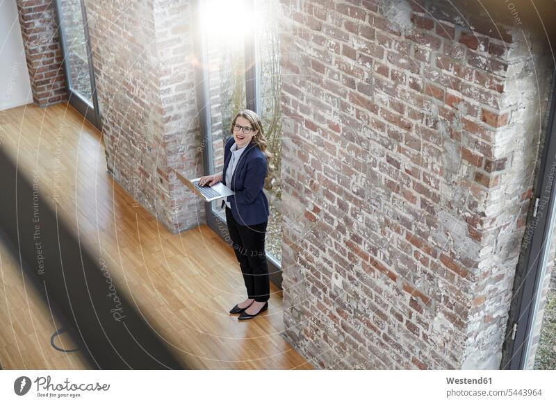 Happy businesswoman on modern office floor using laptop Laptop Computers laptops notebook businesswomen business woman business women computer computers