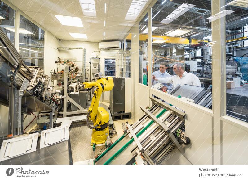 Two men talking in factory shop floor looking at industrial robot factories man males colleagues speaking Adults grown-ups grownups adult people persons