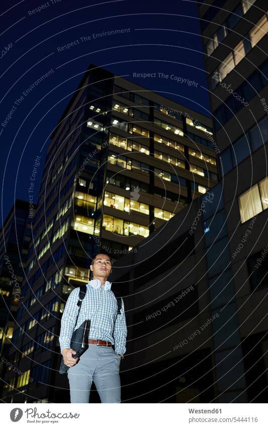 Businessman with folder and headphones walking in the city at night folders file folder town cities towns by night nite night photography men males headset