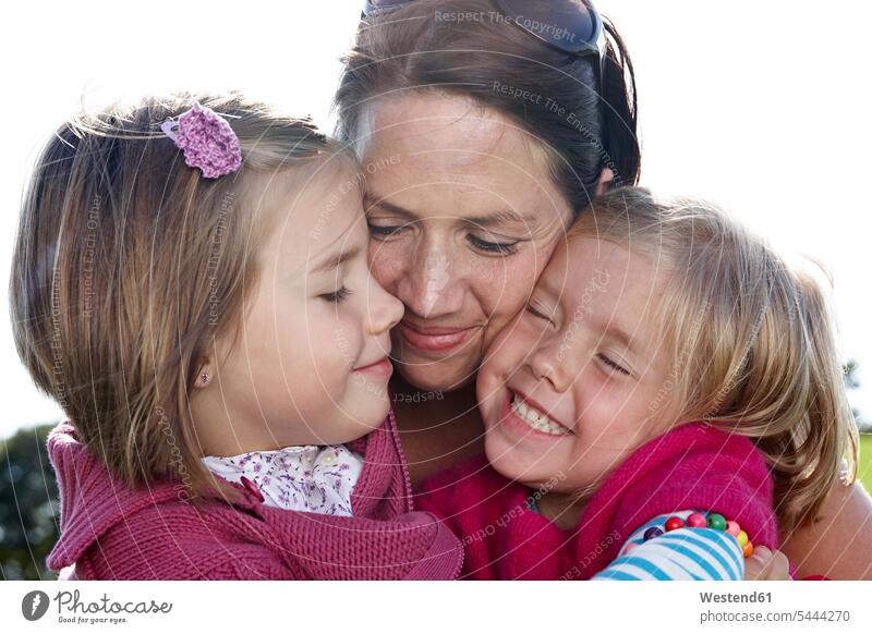 Mother hugging two girls outdoors happiness happy females daughter daughters family families mother mommy mothers mummy mama child children kid kids people