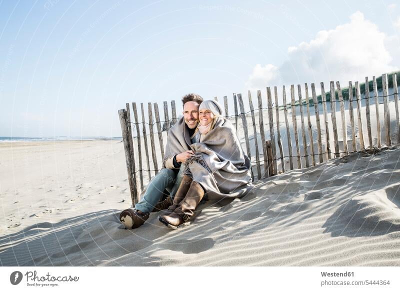 Smiling couple wrapped in blanket on the beach beaches twosomes partnership couples smiling smile people persons human being humans human beings vacation