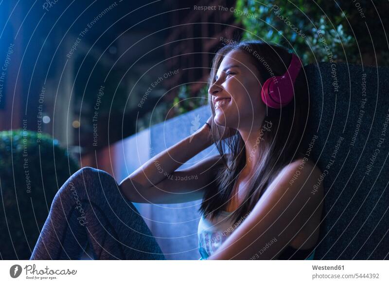 Happy young woman with pink headphones listening to music in modern urban setting at night exercising exercise training practising on the phone call telephoning