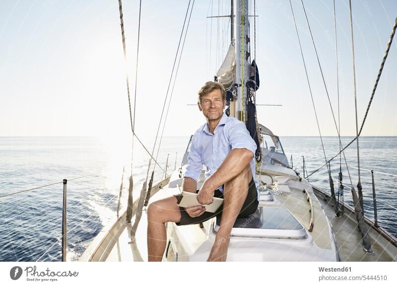 Portrait of smiling mature man with tablet sitting on his sailing boat men males boat sports Adults grown-ups grownups adult people persons human being humans