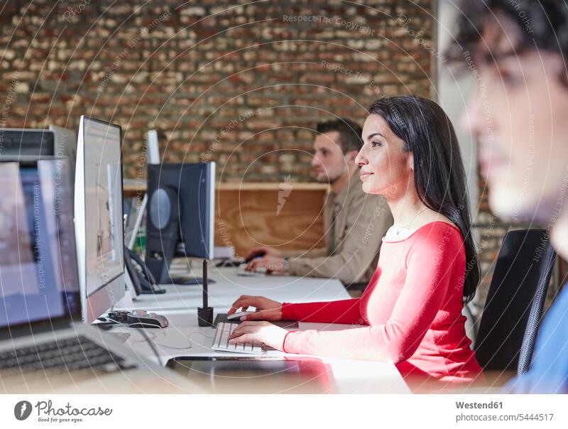 Mature woman working in office with young colleagues offices office room office rooms business people businesspeople computer computers sitting Seated desk