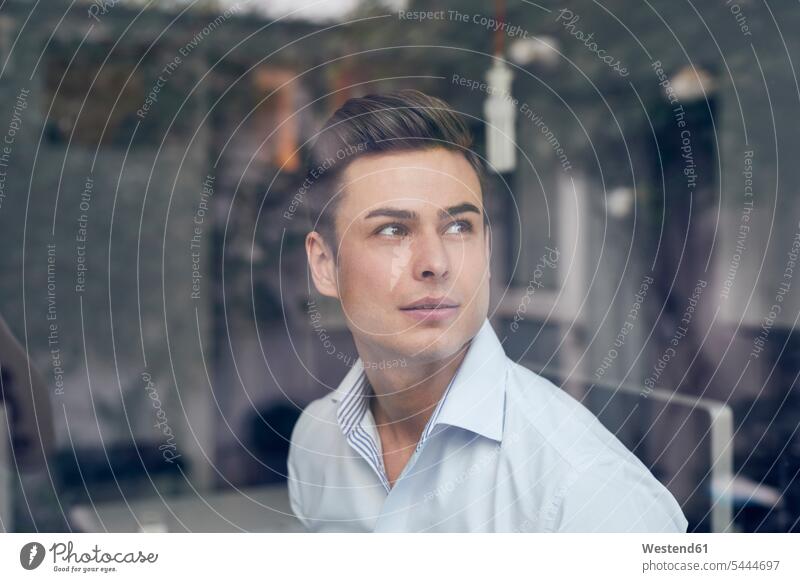 Young businessman behind glass pane in office portrait portraits Businessman Business man Businessmen Business men business people businesspeople business world
