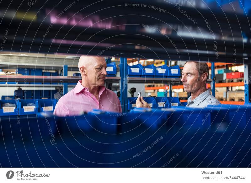 Two men in storehouse examining screw man males talking speaking working At Work factory factories Adults grown-ups grownups adult people persons human being