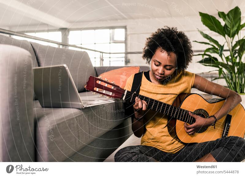 Young woman at home with laptop playing guitar Laptop Computers laptops notebook females women guitars computer computers Adults grown-ups grownups adult people