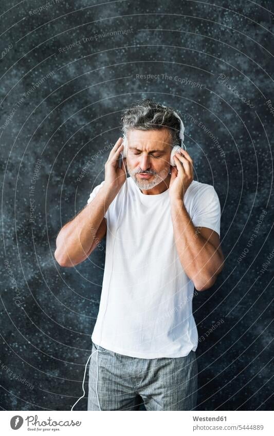 Mature man having fun listening music, wearing headphones headset hearing enjoying indulgence enjoyment savoring indulging standing mature men mature man