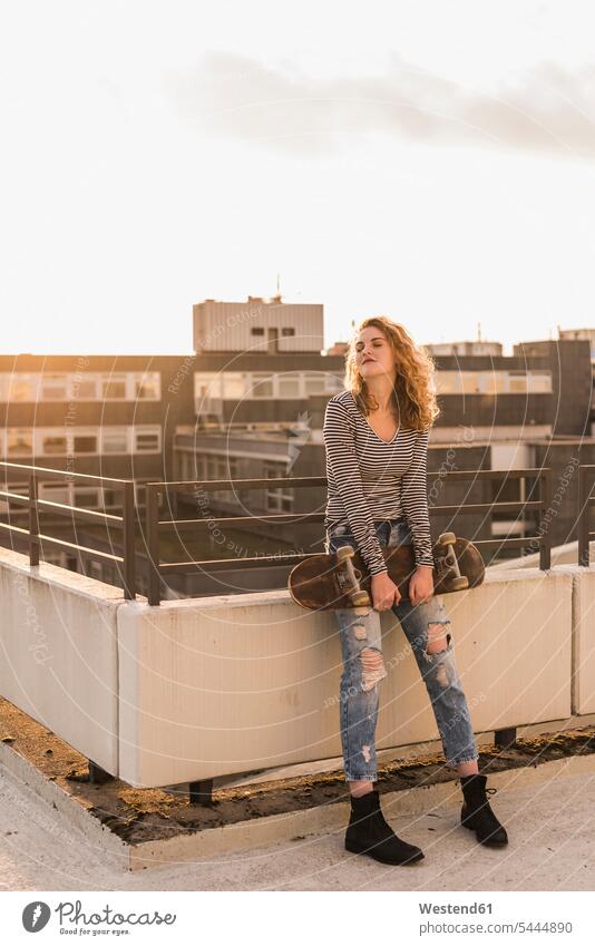 Young woman with skateboard enjoying sunset on roof terrace indulgence enjoyment savoring indulging sunsets sundown females women Skate Board skateboards deck