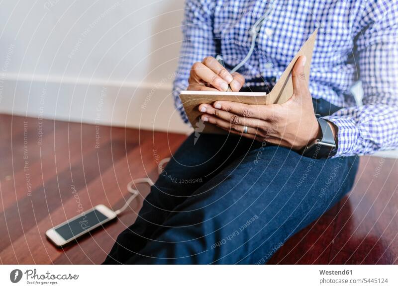 Man sitting on the wooden floor writing a note Seated man men males mobile phone mobiles mobile phones Cellphone cell phone cell phones Businessman Business man