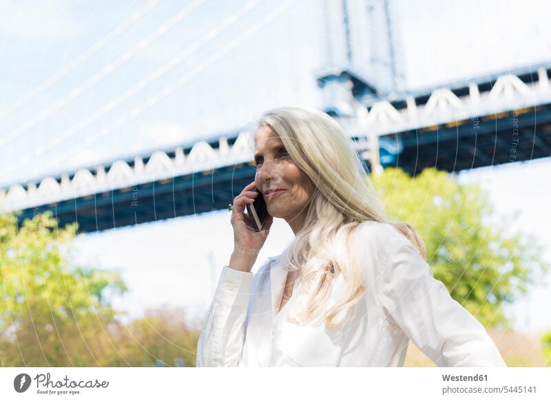 USA, Brooklyn, mature woman on the phone in front of Manhattan Bridge females women call telephoning On The Telephone calling Smartphone iPhone Smartphones