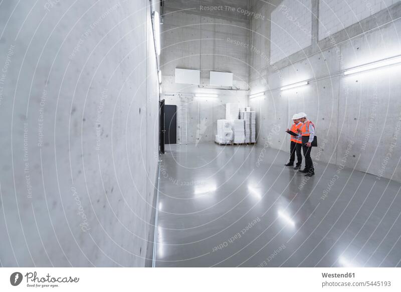 Two colleagues wearing safety vests and hard hats talking in a building man men males working At Work scrutiny scrutinizing Adults grown-ups grownups adult