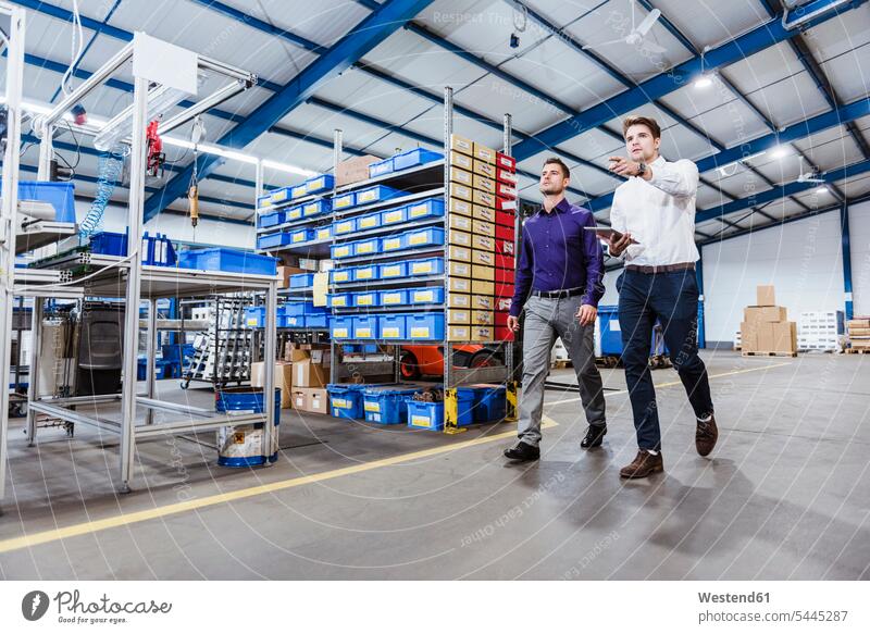 Two business people walking through shop floor. holding digital tablet discussing discussion Meeting Meetings Business Meeting production hall businesspeople