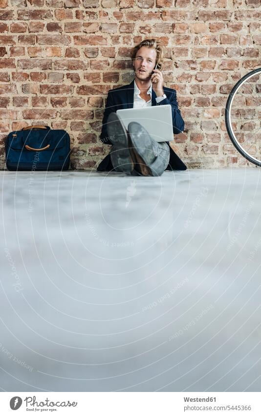 Businessman sitting on floor using laptop and cell phone Laptop Computers laptops notebook men males moving house move Moving Home Seated on the phone call