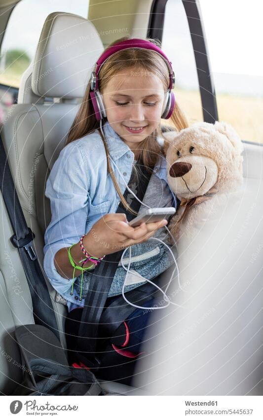 Girl sitting in car, holding teddy bear and listening music girl females girls Road Trip roadtrip Road-Trip vacation Holidays Seated smiling smile hearing