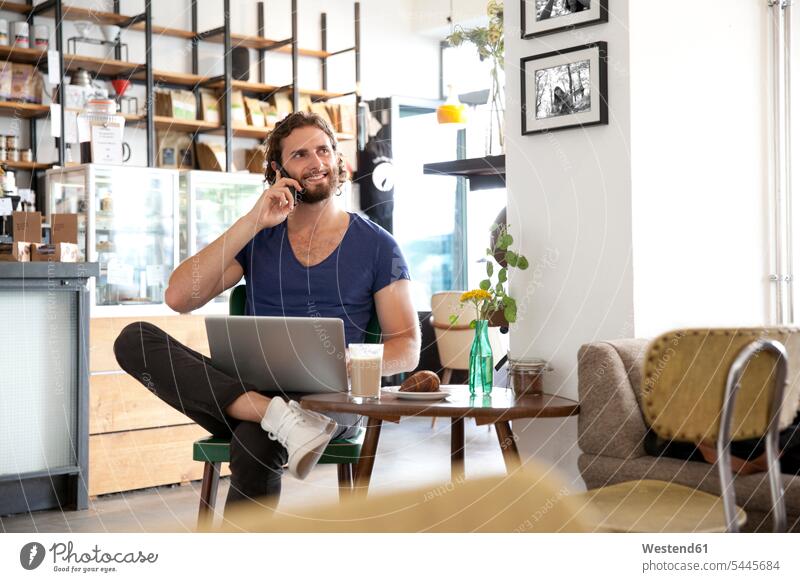 Portrait of young man on the phone sitting in a coffee shop with laptop cafe portrait portraits call telephoning On The Telephone calling men males