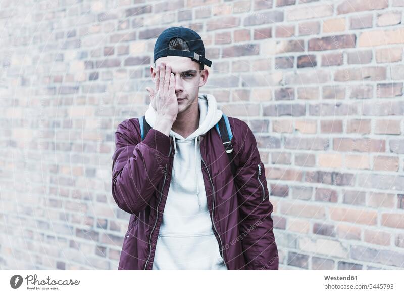 Portrait of young man in front of brick wall covering one eye men males serious earnest Seriousness austere portrait portraits Adults grown-ups grownups adult