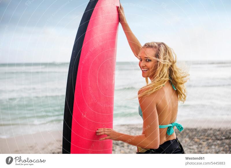 Smiling woman on beach with surfboard beaches surfboards surfing surf ride surf riding Surfboarding females women water sports Water Sport aquatics Adults