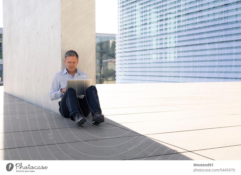 Businessman using laptop outdoors sitting Seated Laptop Computers laptops notebook Business man Businessmen Business men working At Work computer computers