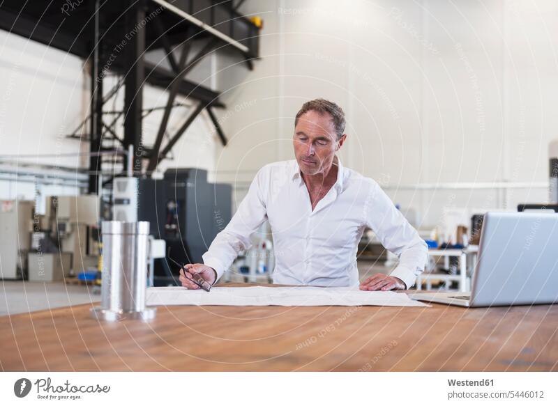 Man looking at plan on table in factory laptop Laptop Computers laptops notebook factories plans Businessman Business man Businessmen Business men computer