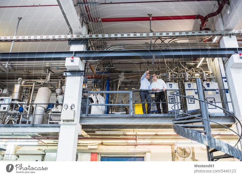 Two men talking in factory shop floor speaking colleagues man males factories Adults grown-ups grownups adult people persons human being humans human beings