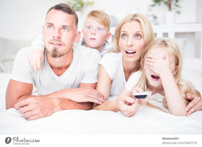 Happy family lying in bed watching Tv laying down lie lying down watching TV Looking At Tv watching television relaxed relaxation families portrait portraits