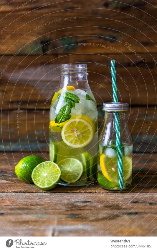 Glass bottles of infused water with lemon, lime, mint leaves and ice cubes ice-cooled iced garnished fruit rich in vitamines Slice Slices half halves halved