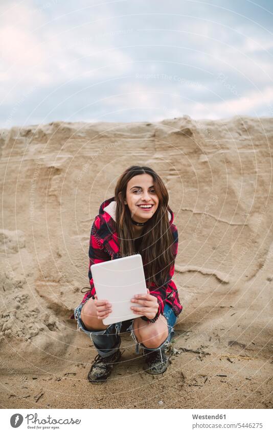 Portrait of smiling young woman with tablet crouching on the beach portrait portraits females women digitizer Tablet Computer Tablet PC Tablet Computers iPad