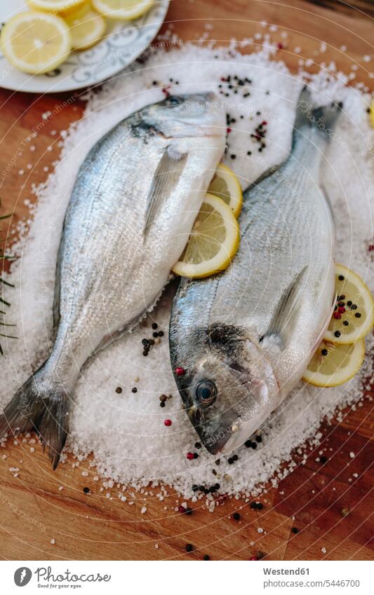 Sea Breams on a wooden board surrounded by salt grains sea bream sea breams Lemon Lemons Slice Slices bird's eye view from above Birds-Eye Perspective top view