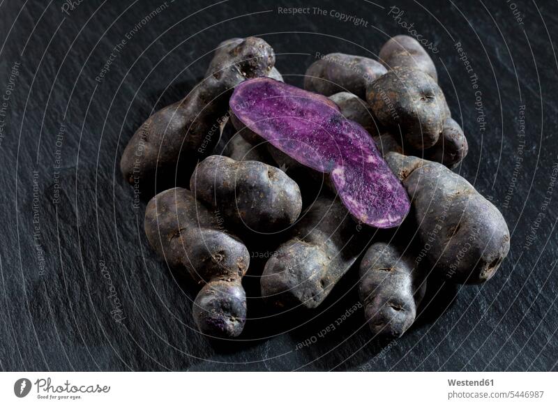 Whole and sliced purple potatoes on slate uncooked Raw Potato Raw Potatoes schist slates half halves halved close-up close up closeups close ups close-ups